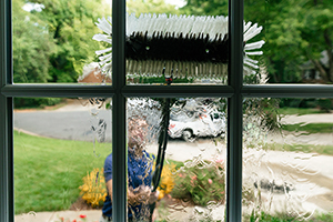 A Window Hero professional uses specialized equipment to clean a ground floor window of a home, as seen from inside.
