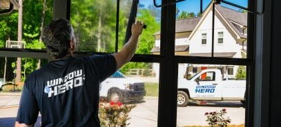 A Window Hero professional inside a home, cleaning a ground floor window with a squeegee.