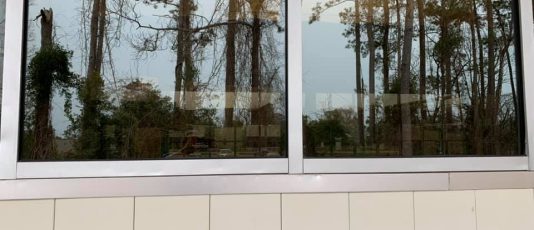 A Window Hero professional uses specialized equipment to clean a ground floor window of a home, as seen from inside.