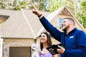 A smiling Window Hero professional points towards a home to show something to the homeowner stood next to him.